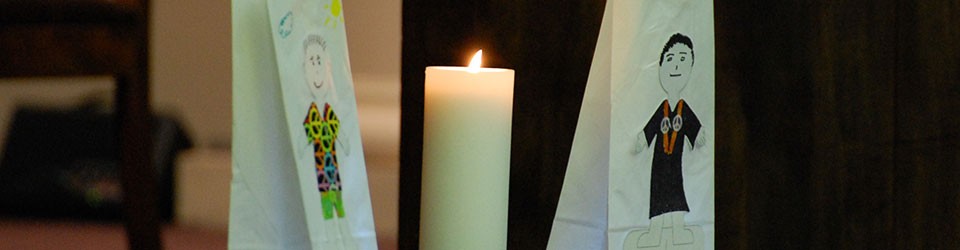 candle with paper sacks on either side featuring figures adorned with peace symbols