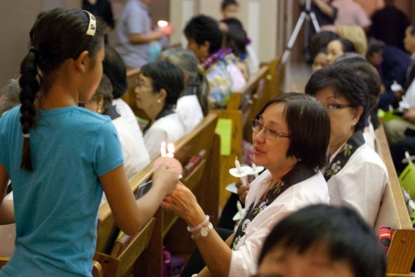 a girl uses one candle to light another held by a Betsuin choir member seated in the pews