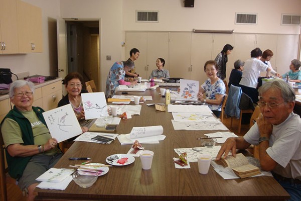Sumie students around a table hold up their work.