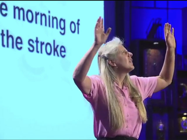 woman holds up both arms with a projected slide with the words "morning of the stroke" behind her