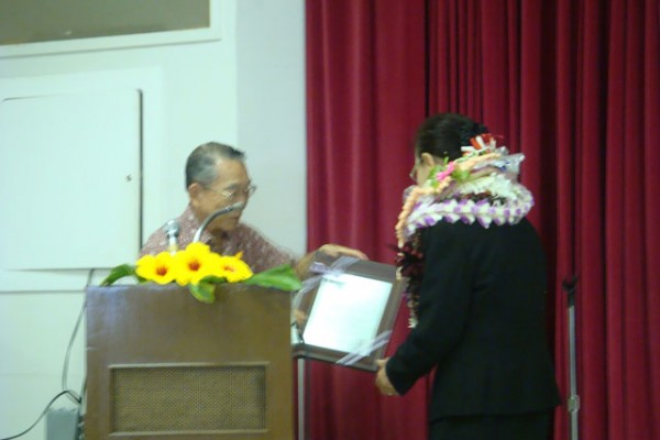 man presents plaque to Mrs. Saito at podium