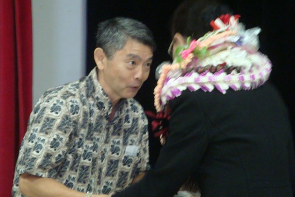 man in Aloha shirt presents envelope to Mrs. Saito