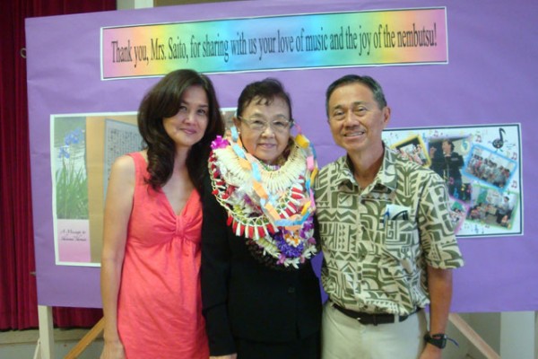 Mrs. Saito with a man and a woman in front of a display board honoring her