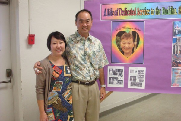 a man and a woman stand by a display board honoring Mrs. Saito