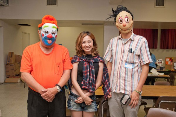 ministers in clown masks on either side of a visitor from Japan