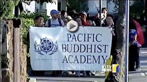 KITV video still showing walkers behind a large banner reading Pacific Buddhist Academy