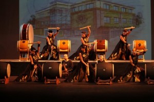 PBA taiko drummers with sketch of planned new school building in background