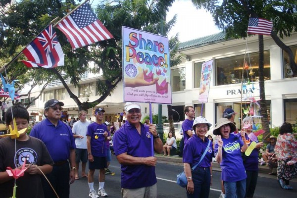 purple-shirted parade participants with flags, origami cranes, and Share Peace signs