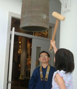 child strikes the a large, Japanese bell with a wooden mallet