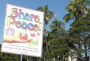 Share Peace in rainbow letters with origami cranes against a background of blue sky and palm trees