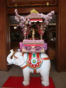Baby Buddha statue in a blossom-adorned shrine atop an elephant