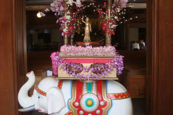 Baby Buddha statue in a blossom-adorned shrine atop an elephant