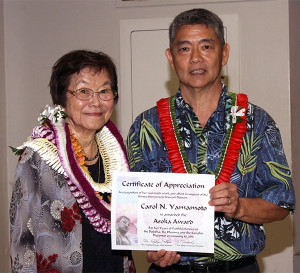 a woman and a man wearing lei holding an award certificate