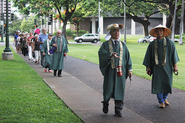 ministers in green robes lead a line of walkers into Honolulu Hale Civic Grounds