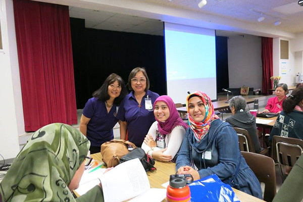 two BWA women in purple shirts with Muslim women wearing hijab in the Social Hall