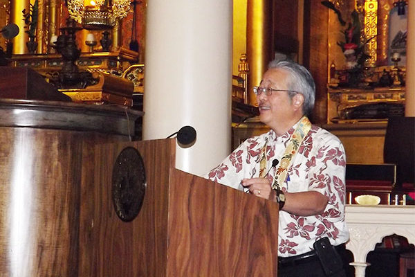 man at lectern with Buddhist altar in the background