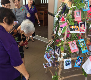 women take a closer look at photos pinned to the "Mother Tree"