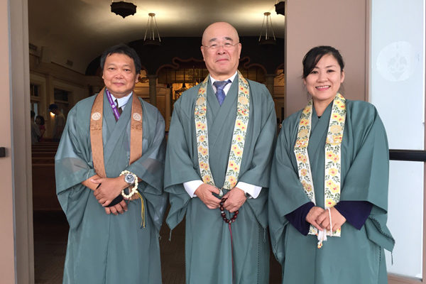three smiling reverends in green robes in front of the main temple hall