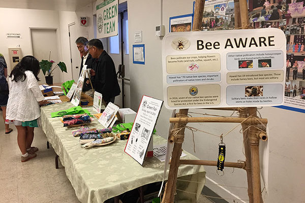 a bamboo "tree" with a "Bee AWARE" sign; utensil kit sales in the background
