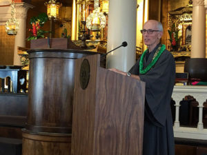 Michael Kieran speaks at the 2019 Earth Day Service wearing robes and a green lei
