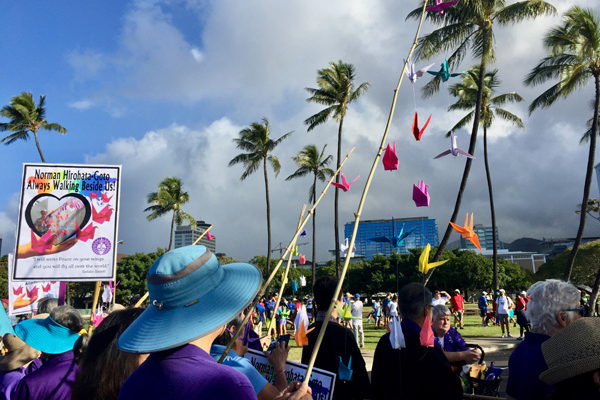 MLK 2020 - group assembles in Magic Island, sign honoring Norman Hirohata-Goto, and origami cranes with background of sky and palm trees
