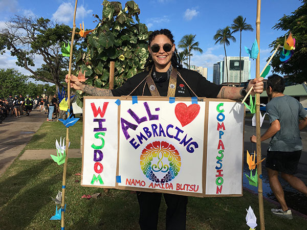 Hawaii Betsuin member with "All-Embracing Wisdom and Compassion" sign with cranes on bamboo poles